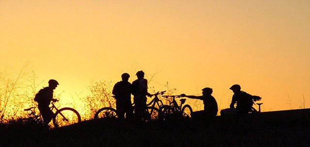 cyclists silhouetted in front of a sunset